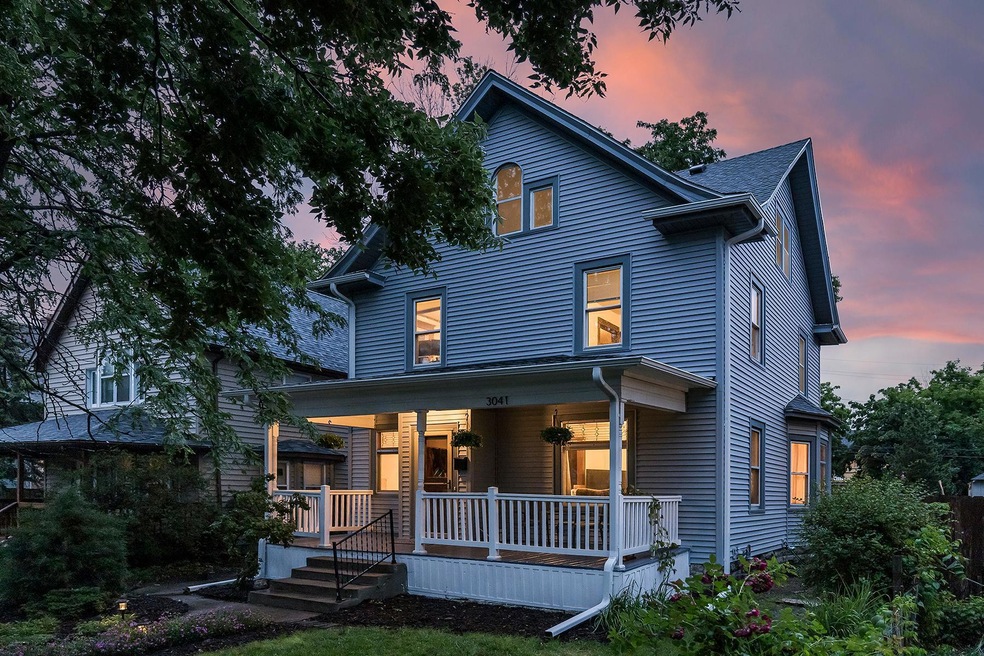 A blue two-storey house at 3041 Elliot Avenue, Minneapolis, with a covered front porch at sunset